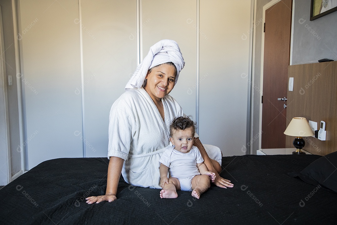 Mãe e seu bebê após banho sentados na cama