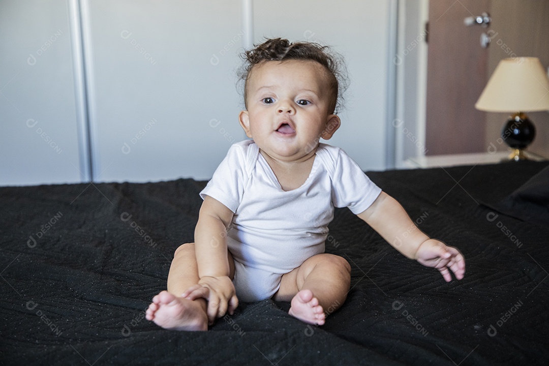 Bebê lindo sentado na cama sorrindo