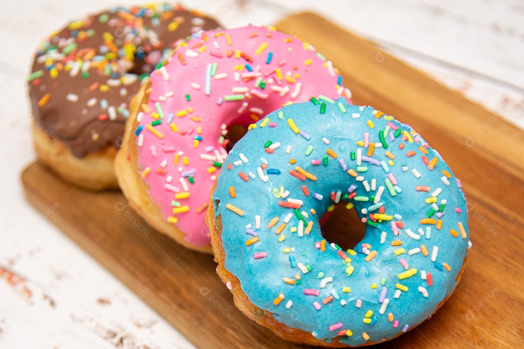 Rosquinhas com cobertura azul rosa e chocolate sobre uma tábua