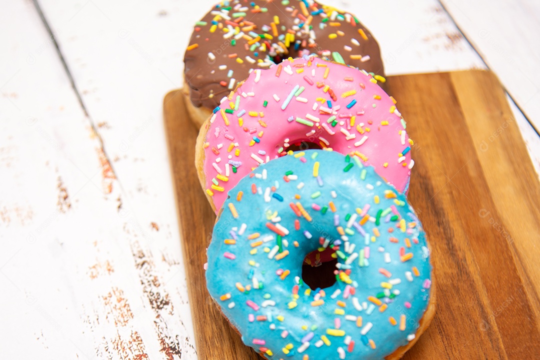 Rosquinhas com cobertura azul rosa e chocolate sobre uma tábua