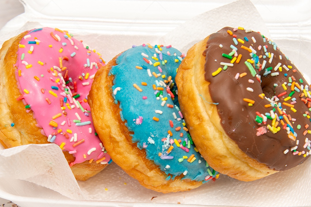 Três donuts delicioso com coberturas coloridas sobre tábua