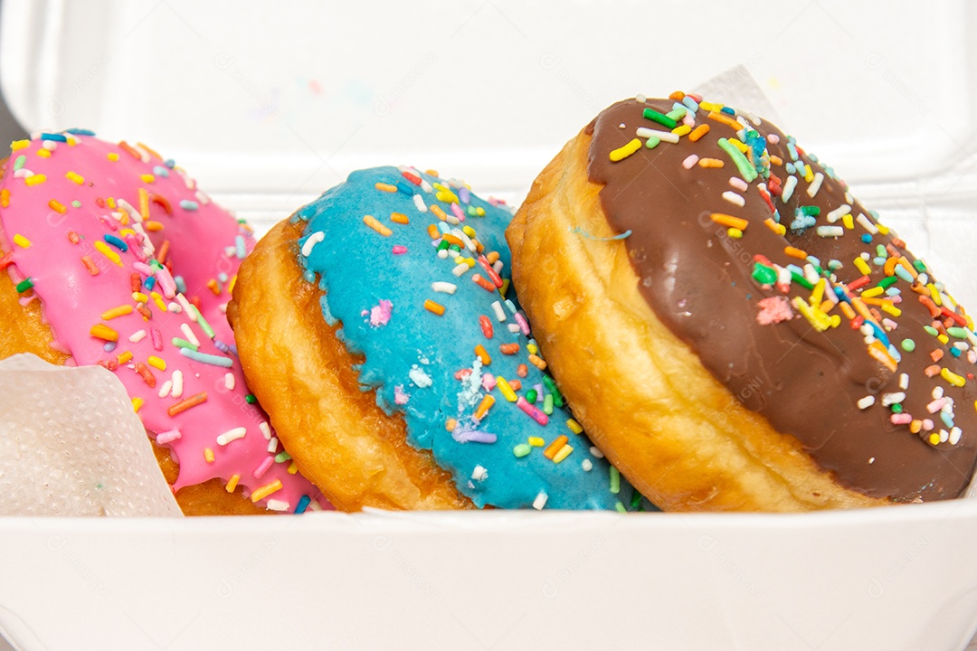 Três donuts delicioso com coberturas coloridas sobre tábua