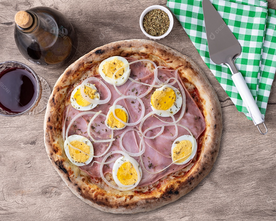 Pizza portuguesa sobre mesa de madeira com vinho ao lado