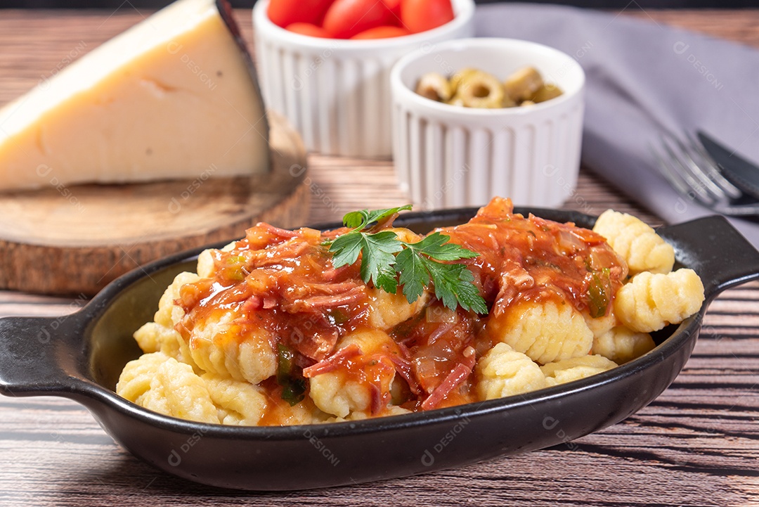 Nhoque com queijo parmesão ao lado em molho de tomate sobre uma mesa de madeira