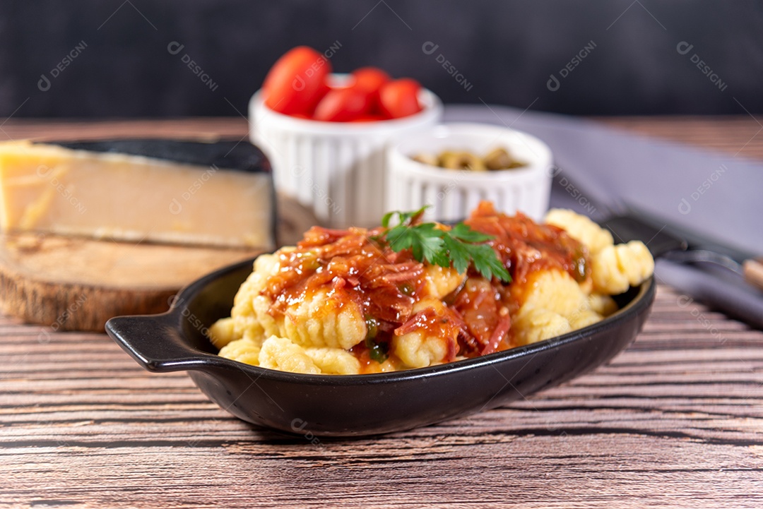 Nhoque com queijo parmesão ao lado em molho de tomate sobre uma mesa de madeira