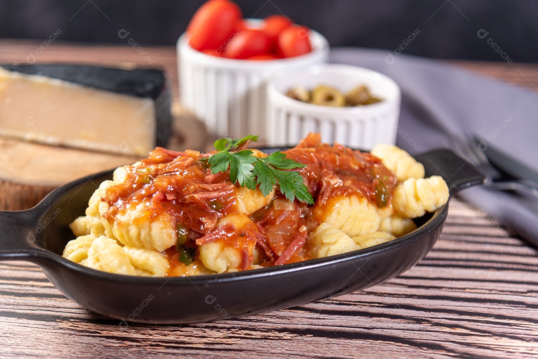 Nhoque com queijo parmesão ao lado em molho de tomate sobre uma mesa de madeira