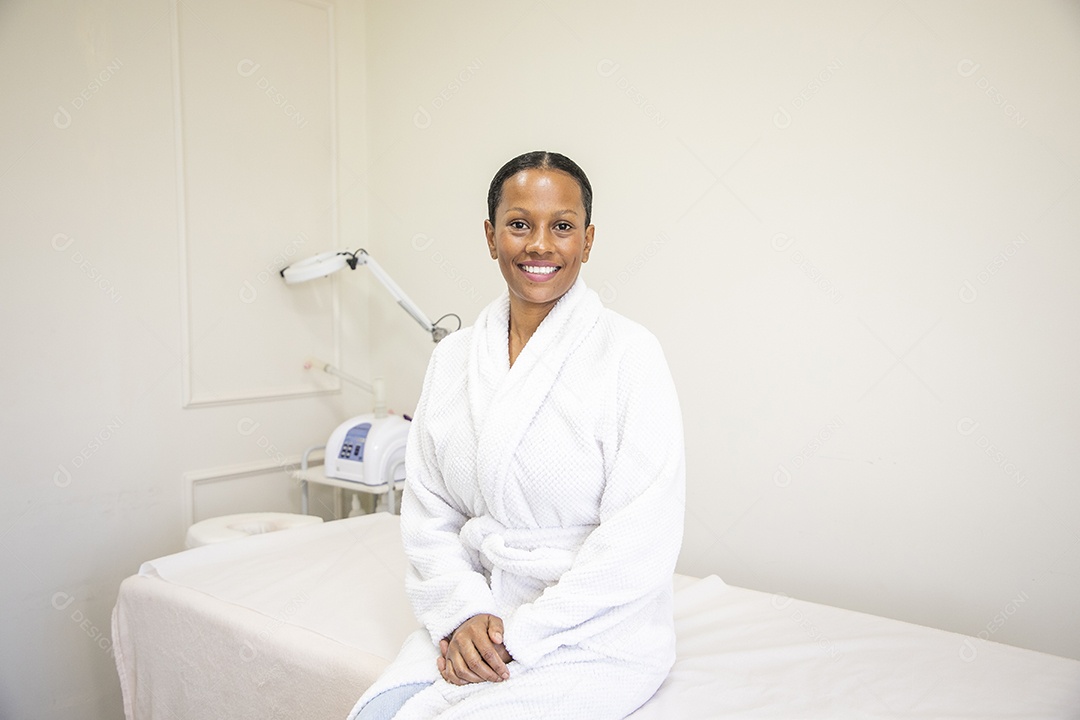 Mulher morena de roupão sorrindo sentada na maca