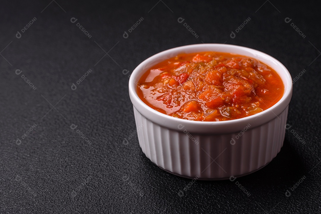 Molho encarnado ou picante com pimenta, tomate, alho, especiarias e ervas em um fundo escuro de concreto
