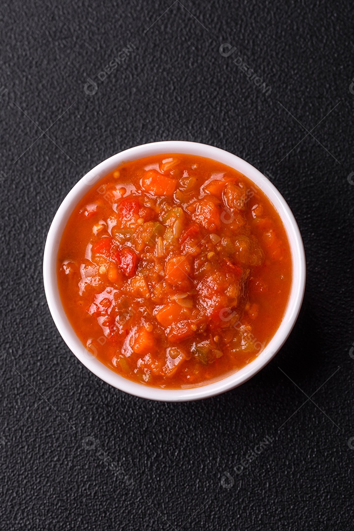 Molho encarnado ou picante com pimenta, tomate, alho, especiarias e ervas em um fundo escuro de concreto