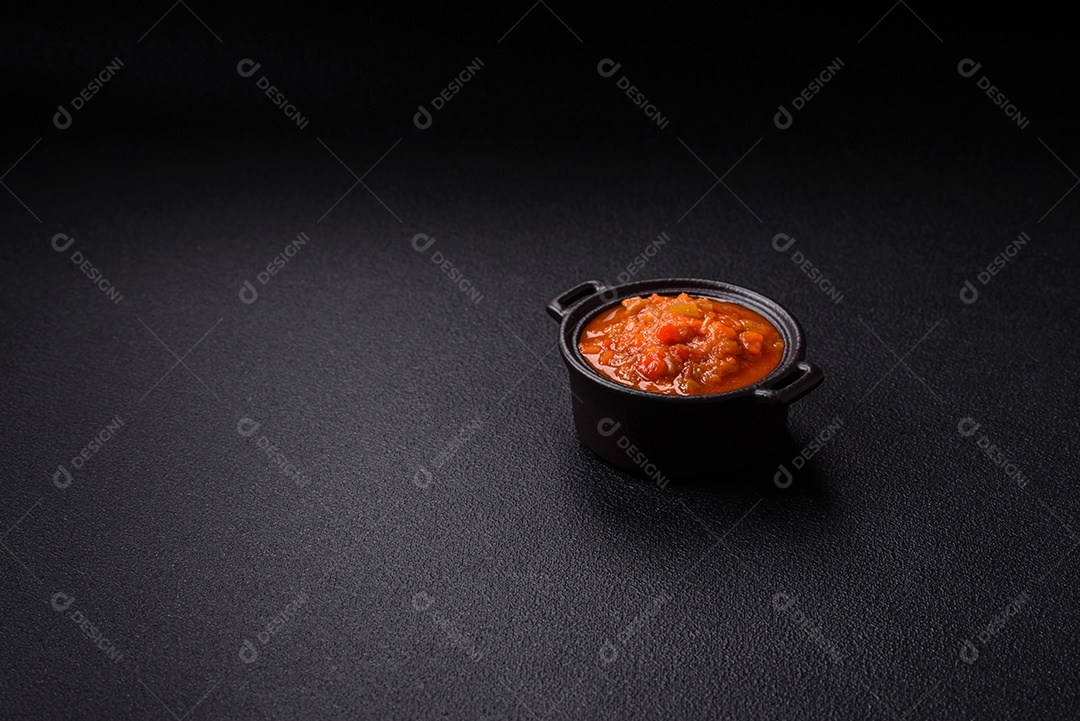 Molho encarnado ou picante com pimenta, tomate, alho, especiarias e ervas em um fundo escuro de concreto
