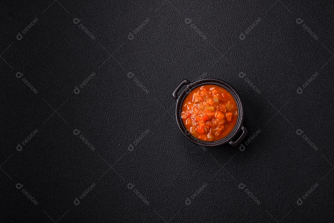 Molho encarnado ou picante com pimenta, tomate, alho, especiarias e ervas em um fundo escuro de concreto