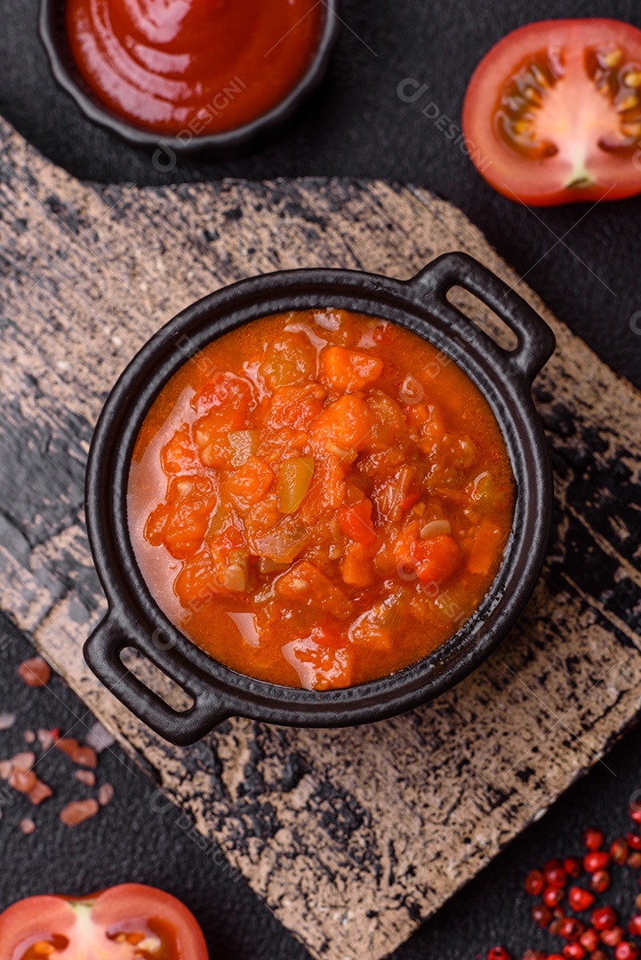Molho encarnado ou picante com pimenta, tomate, alho, especiarias e ervas em um fundo escuro de concreto
