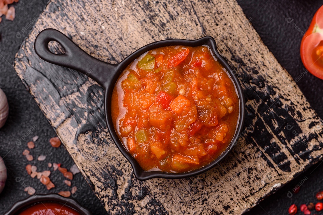 Molho encarnado ou picante com pimenta, tomate, alho, especiarias e ervas em um fundo escuro de concreto