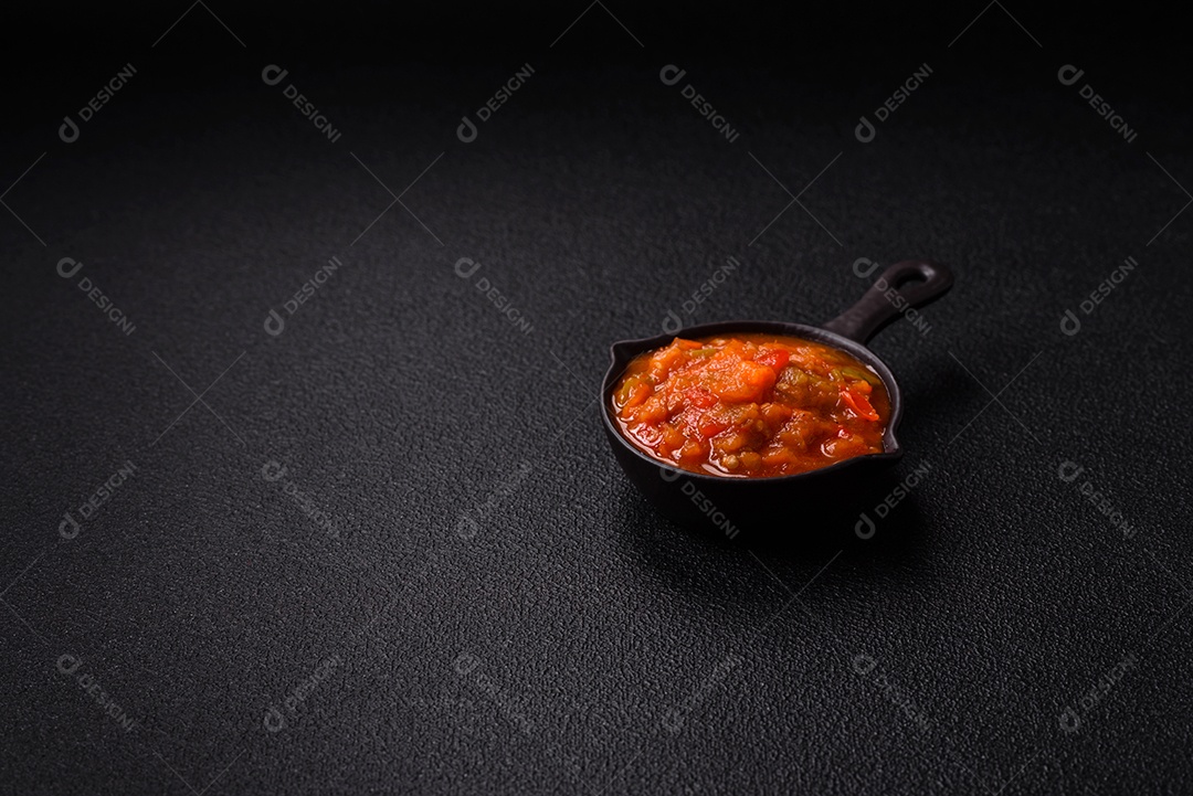 Molho encarnado ou picante com pimenta, tomate, alho, especiarias e ervas em um fundo escuro de concreto