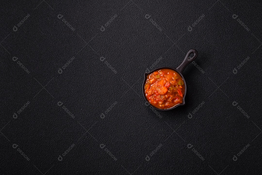 Molho encarnado ou picante com pimenta, tomate, alho, especiarias e ervas em um fundo escuro de concreto