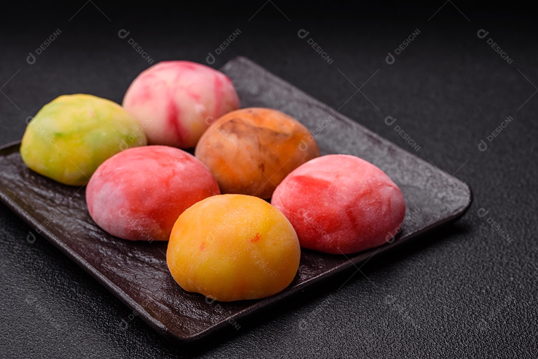 Deliciosos doces mochi asiáticos coloridos com casca de massa de arroz e recheio de frutas em fundo escuro de concreto