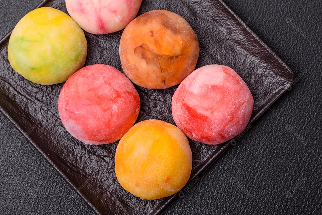 Deliciosos doces mochi asiáticos coloridos com casca de massa de arroz e recheio de frutas em fundo escuro de concreto