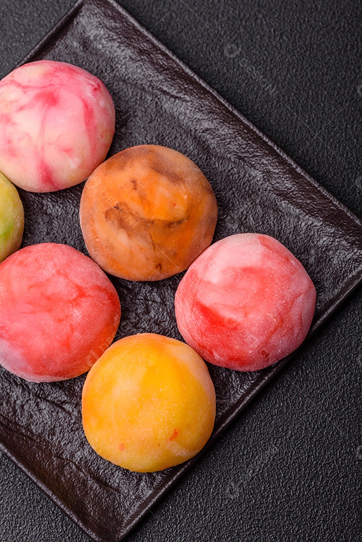 Deliciosos doces mochi asiáticos coloridos com casca de massa de arroz e recheio de frutas em fundo escuro de concreto