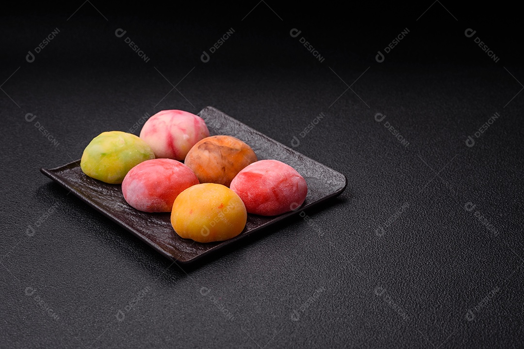Deliciosos doces mochi asiáticos coloridos com casca de massa de arroz e recheio de frutas em fundo escuro de concreto