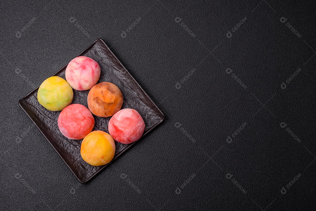 Deliciosos doces mochi asiáticos coloridos com casca de massa de arroz e recheio de frutas em fundo escuro de concreto