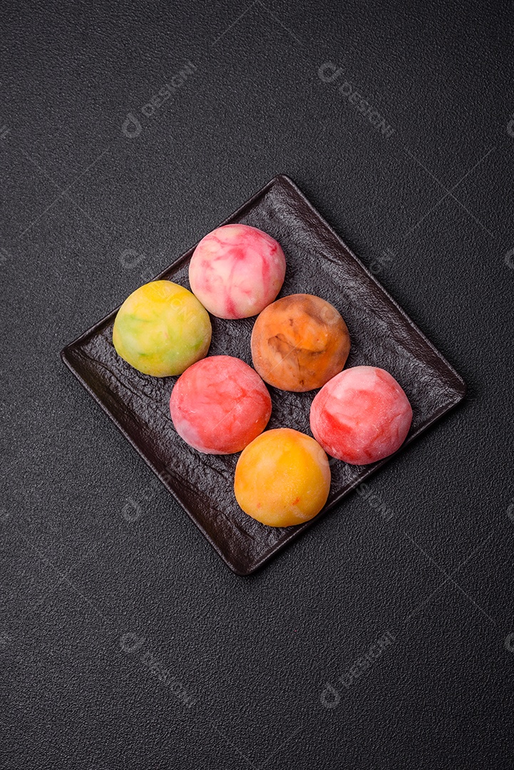Deliciosos doces mochi asiáticos coloridos com casca de massa de arroz e recheio de frutas em fundo escuro de concreto