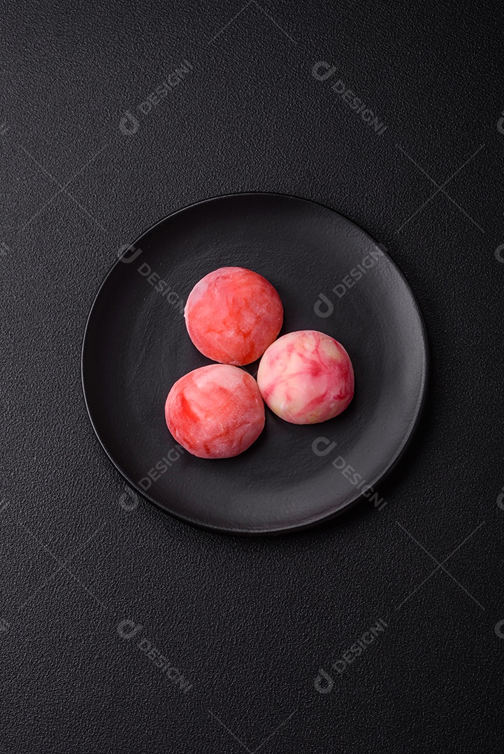 Deliciosos doces mochi asiáticos coloridos com casca de massa de arroz e recheio de frutas em fundo escuro de concreto