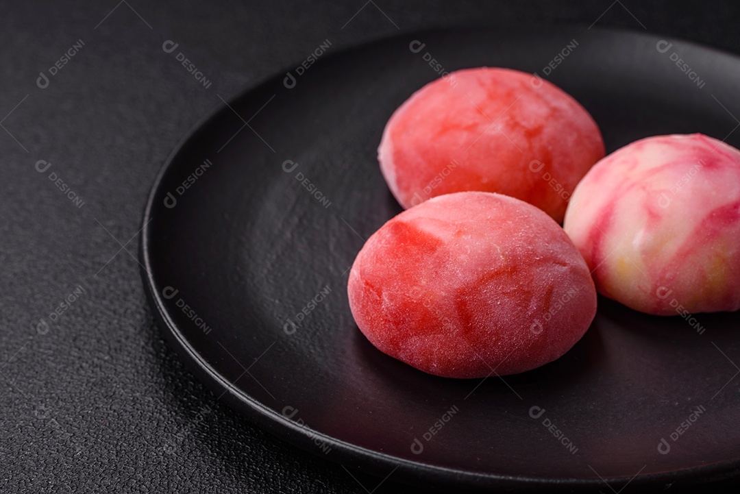 Deliciosos doces mochi asiáticos coloridos com casca de massa de arroz e recheio de frutas em fundo escuro de concreto