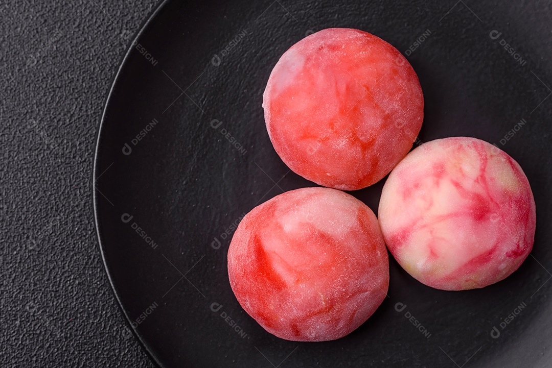 Deliciosos doces mochi asiáticos coloridos com casca de massa de arroz e recheio de frutas em fundo escuro de concreto