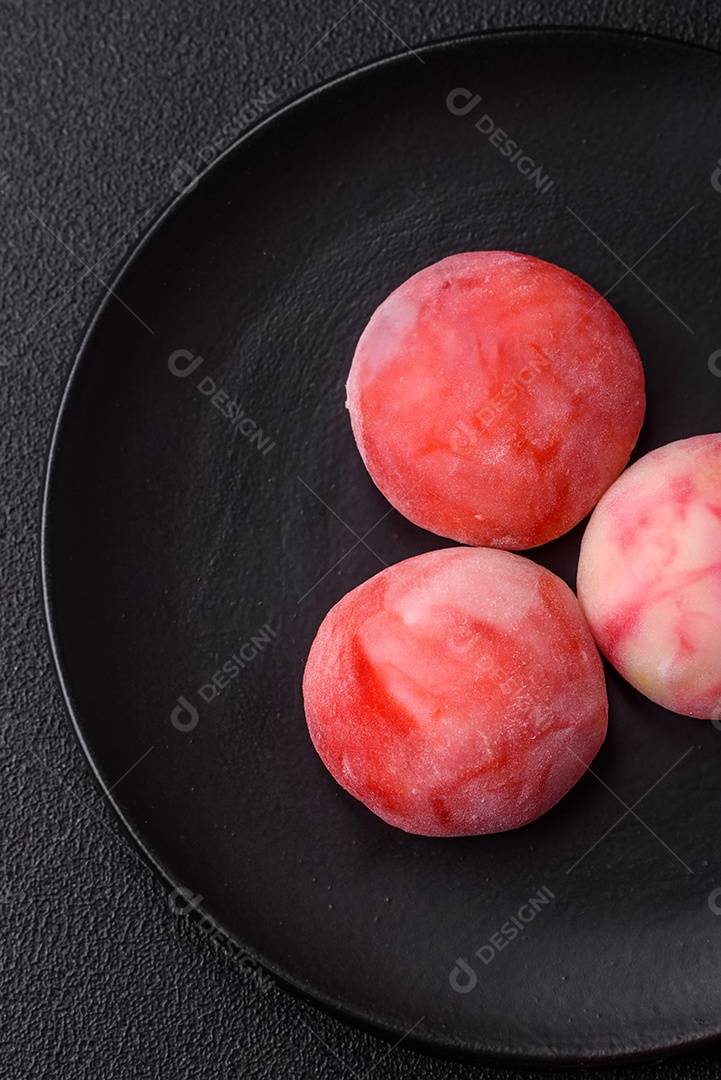 Deliciosos doces mochi asiáticos coloridos com casca de massa de arroz e recheio de frutas em fundo escuro de concreto