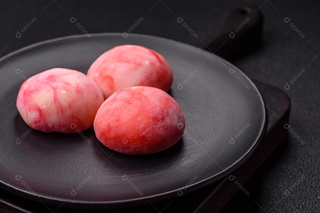 Deliciosos doces mochi asiáticos coloridos com casca de massa de arroz e recheio de frutas em fundo escuro de concreto