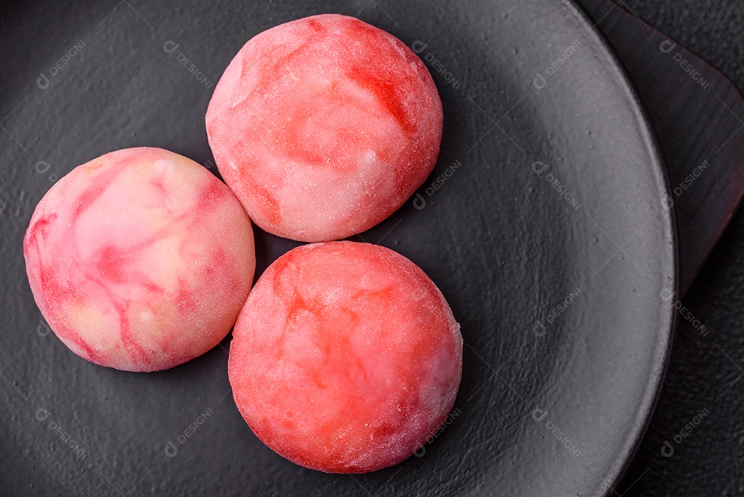 Deliciosos doces mochi asiáticos coloridos com casca de massa de arroz e recheio de frutas em fundo escuro de concreto