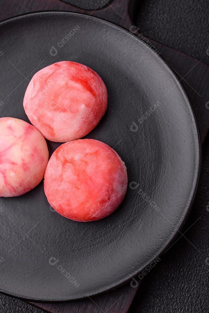 Deliciosos doces mochi asiáticos coloridos com casca de massa de arroz e recheio de frutas em fundo escuro de concreto