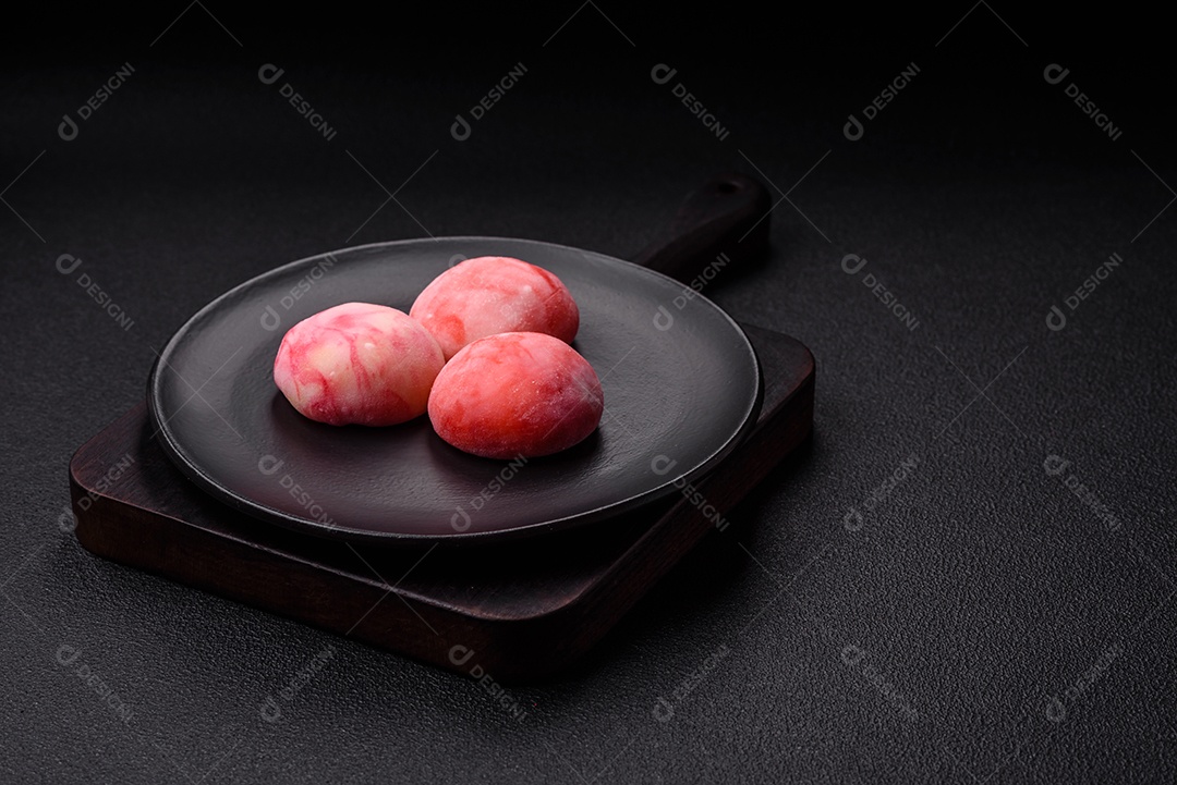 Deliciosos doces mochi asiáticos coloridos com casca de massa de arroz e recheio de frutas em fundo escuro de concreto