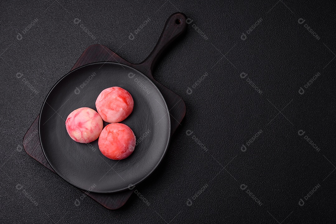 Deliciosos doces mochi asiáticos coloridos com casca de massa de arroz e recheio de frutas em fundo escuro de concreto