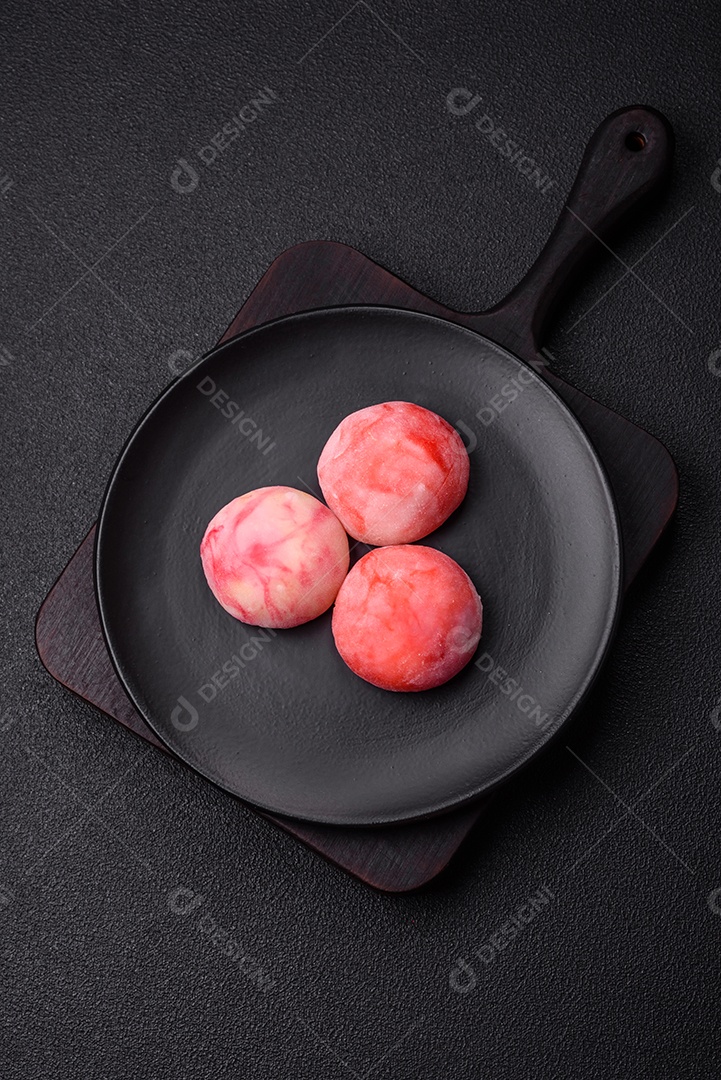 Deliciosos doces mochi asiáticos coloridos com casca de massa de arroz e recheio de frutas em fundo escuro de concreto