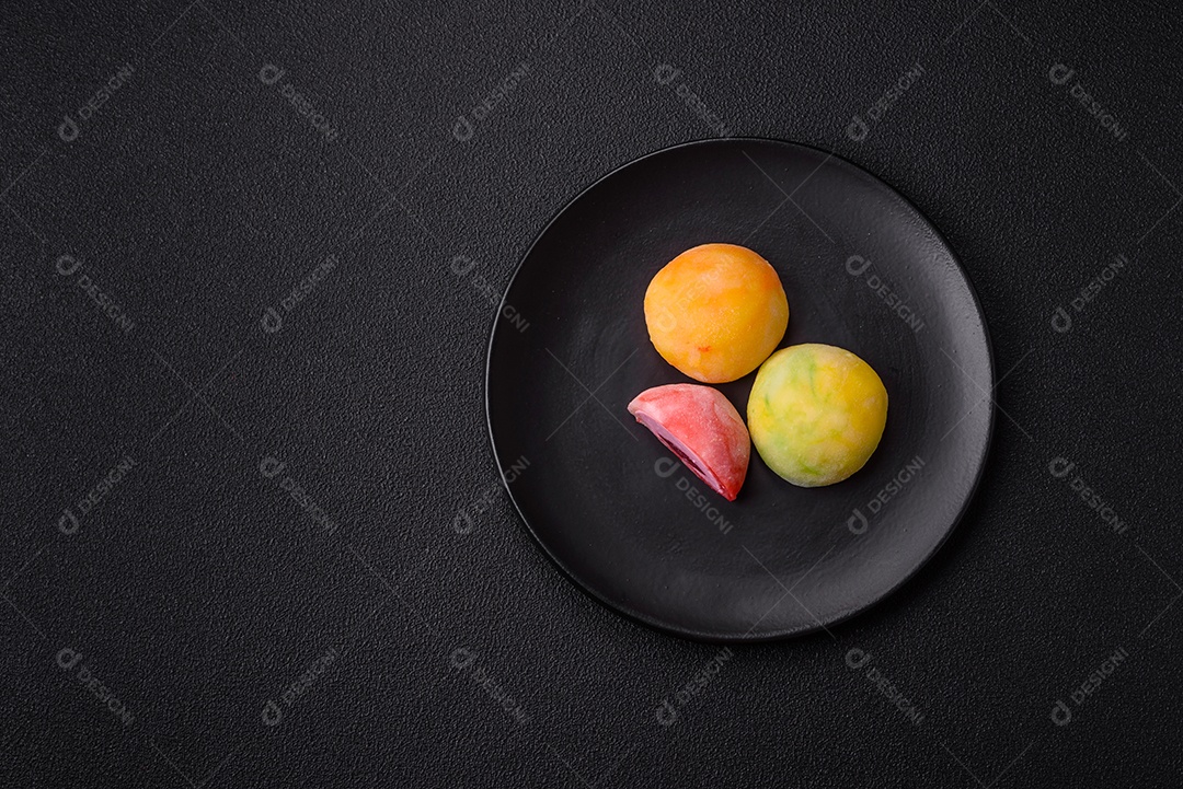 Deliciosos doces mochi asiáticos coloridos com casca de massa de arroz e recheio de frutas em fundo escuro de concreto