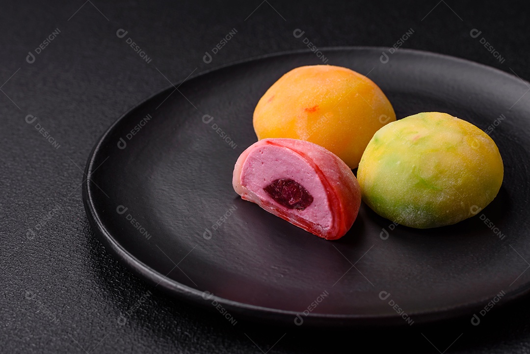 Deliciosos doces mochi asiáticos coloridos com casca de massa de arroz e recheio de frutas em fundo escuro de concreto