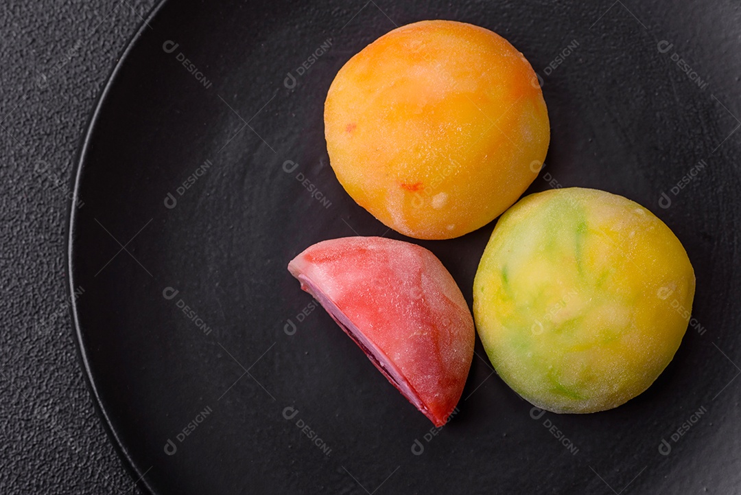 Deliciosos doces mochi asiáticos coloridos com casca de massa de arroz e recheio de frutas em fundo escuro de concreto