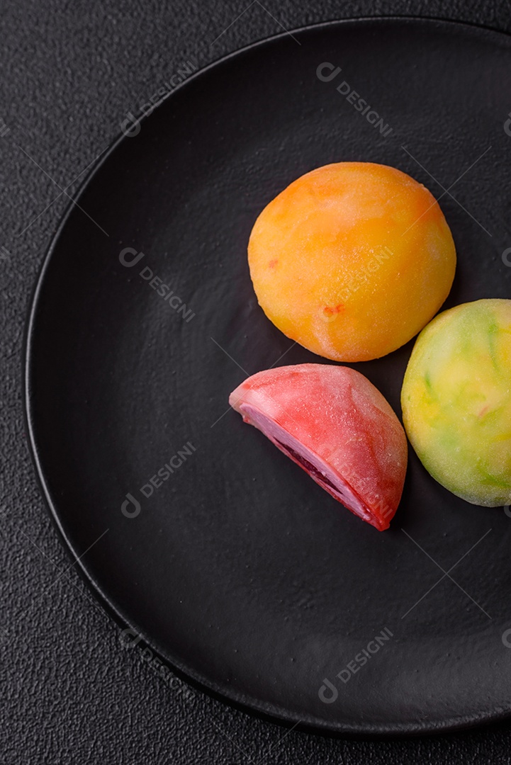 Deliciosos doces mochi asiáticos coloridos com casca de massa de arroz e recheio de frutas em fundo escuro de concreto