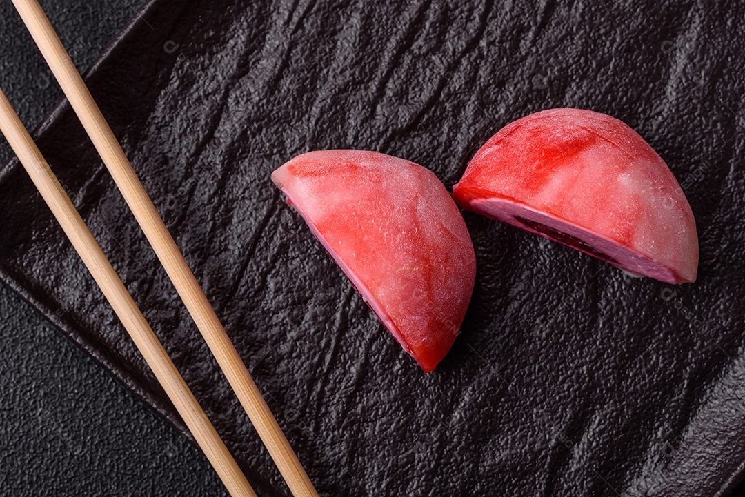 Deliciosos doces mochi asiáticos coloridos com casca de massa de arroz e recheio de frutas em fundo escuro de concreto