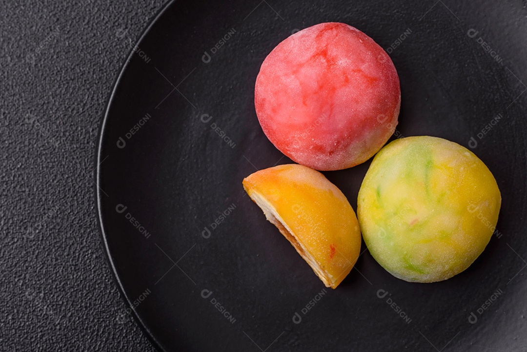 Deliciosos doces mochi asiáticos coloridos com casca de massa de arroz e recheio de frutas em fundo escuro de concreto