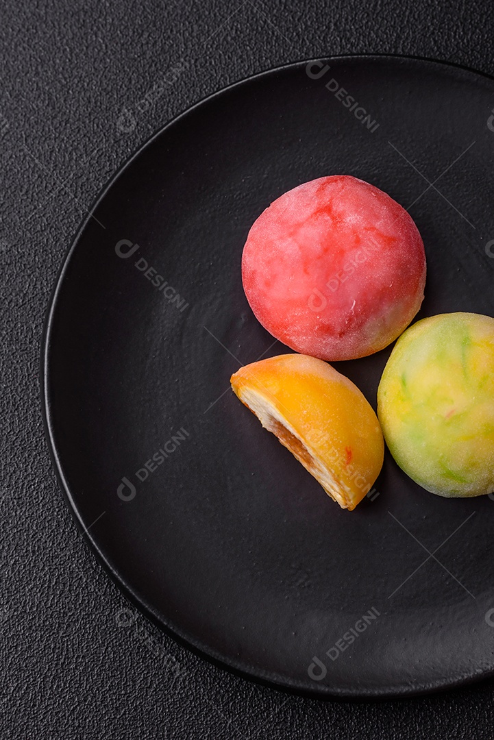 Deliciosos doces mochi asiáticos coloridos com casca de massa de arroz e recheio de frutas em fundo escuro de concreto