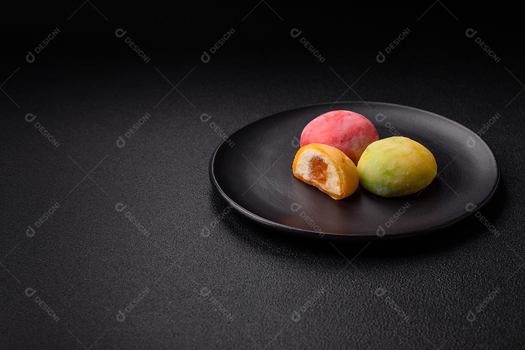 Deliciosos doces mochi asiáticos coloridos com casca de massa de arroz e recheio de frutas em fundo escuro de concreto