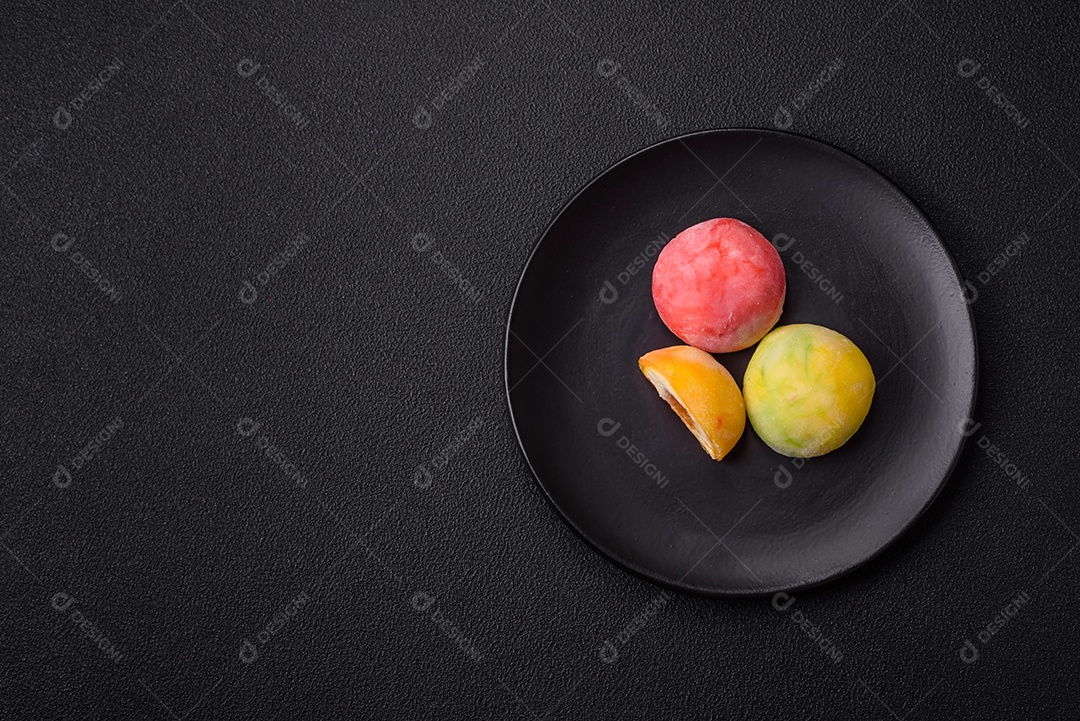 Deliciosos doces mochi asiáticos coloridos com casca de massa de arroz e recheio de frutas em fundo escuro de concreto