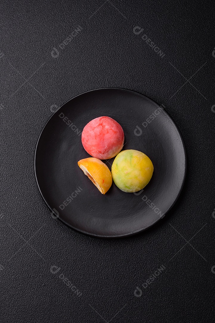 Deliciosos doces mochi asiáticos coloridos com casca de massa de arroz e recheio de frutas em fundo escuro de concreto