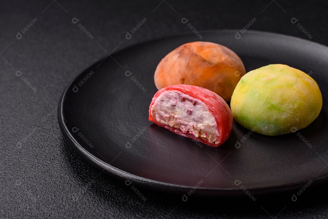 Deliciosos doces mochi asiáticos coloridos com casca de massa de arroz e recheio de frutas em fundo escuro de concreto