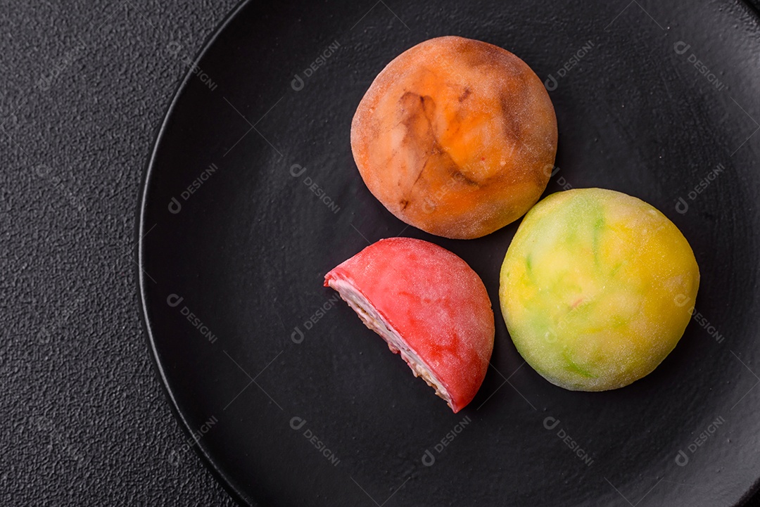 Deliciosos doces mochi asiáticos coloridos com casca de massa de arroz e recheio de frutas em fundo escuro de concreto