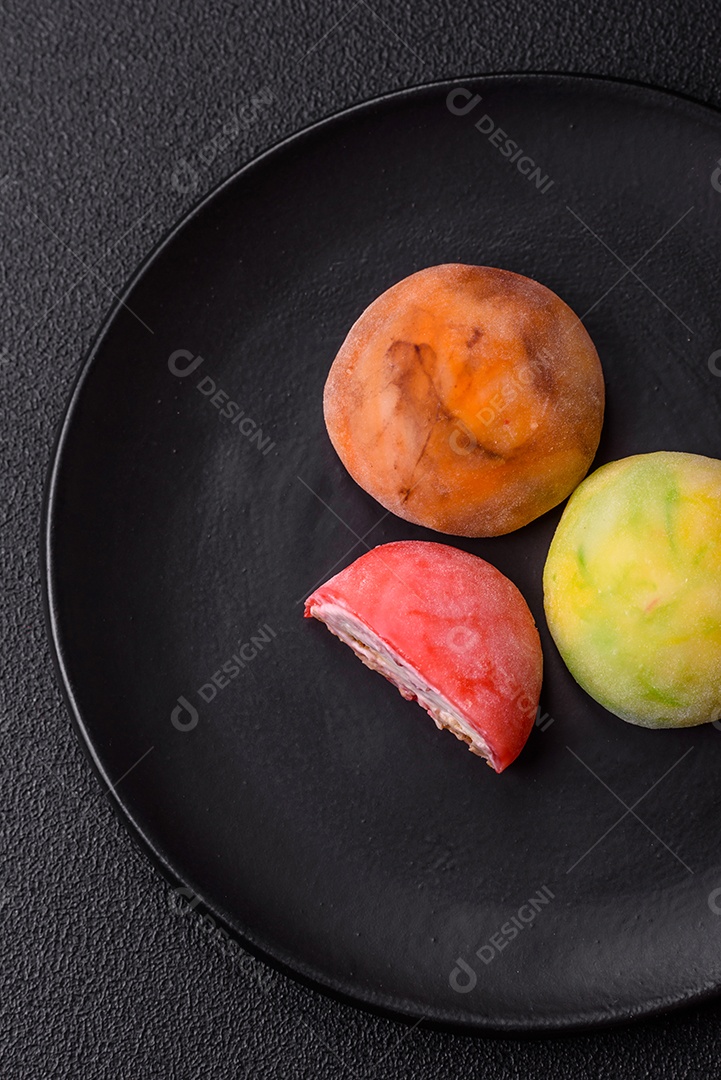 Deliciosos doces mochi asiáticos coloridos com casca de massa de arroz e recheio de frutas em fundo escuro de concreto