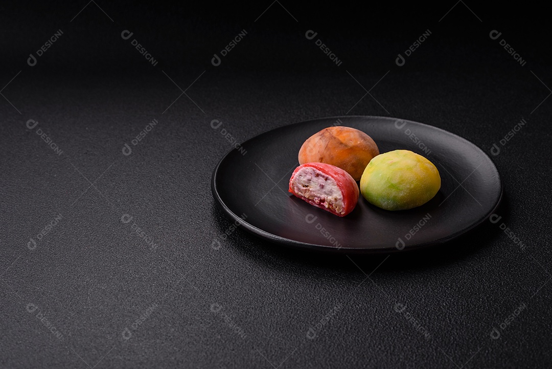 Deliciosos doces mochi asiáticos coloridos com casca de massa de arroz e recheio de frutas em fundo escuro de concreto