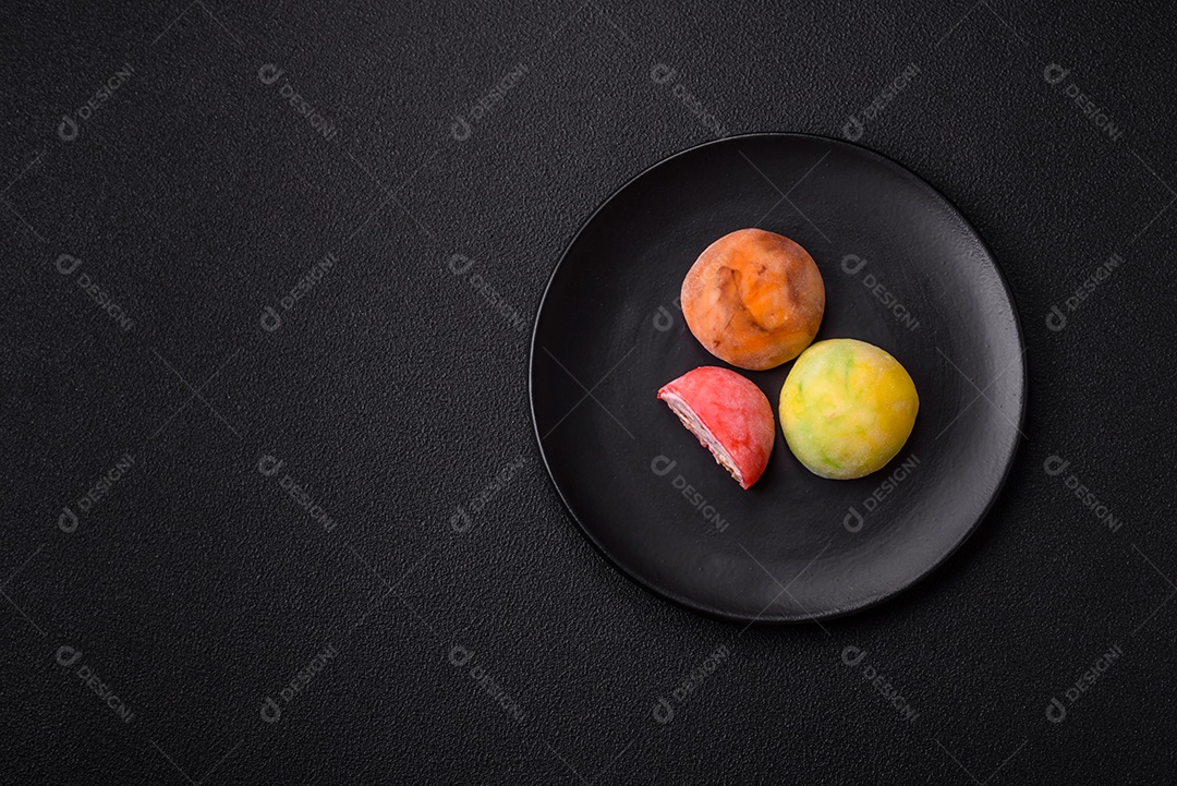 Deliciosos doces mochi asiáticos coloridos com casca de massa de arroz e recheio de frutas em fundo escuro de concret